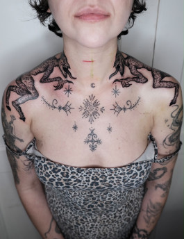 Körperangepasste Tattoo-Komposition von Jette mit zwei dunklen Kreaturen entlang der Schultern sowie feinen ornamentalen und sternartigen Symbolen auf Brust und Hals.
