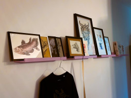 Gerahmte Kunstwerke und Illustrationen auf einem Wandregal im Beechhouse Tattoo Studio in Bochum.